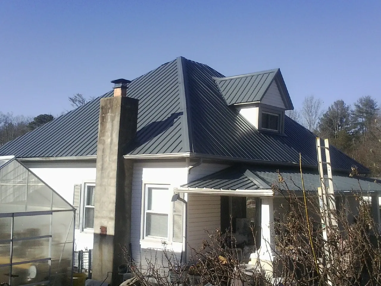 Dark blue standing seam metal roof on a white farmhouse with dormer — Slate & Tile Roof Repair by Roofing Brothers in Ionia