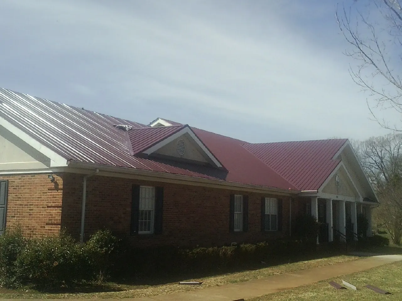 Red metal roof with gabled entries on a long brick building, from a Hail Damage Roof Repair job in Ionia
