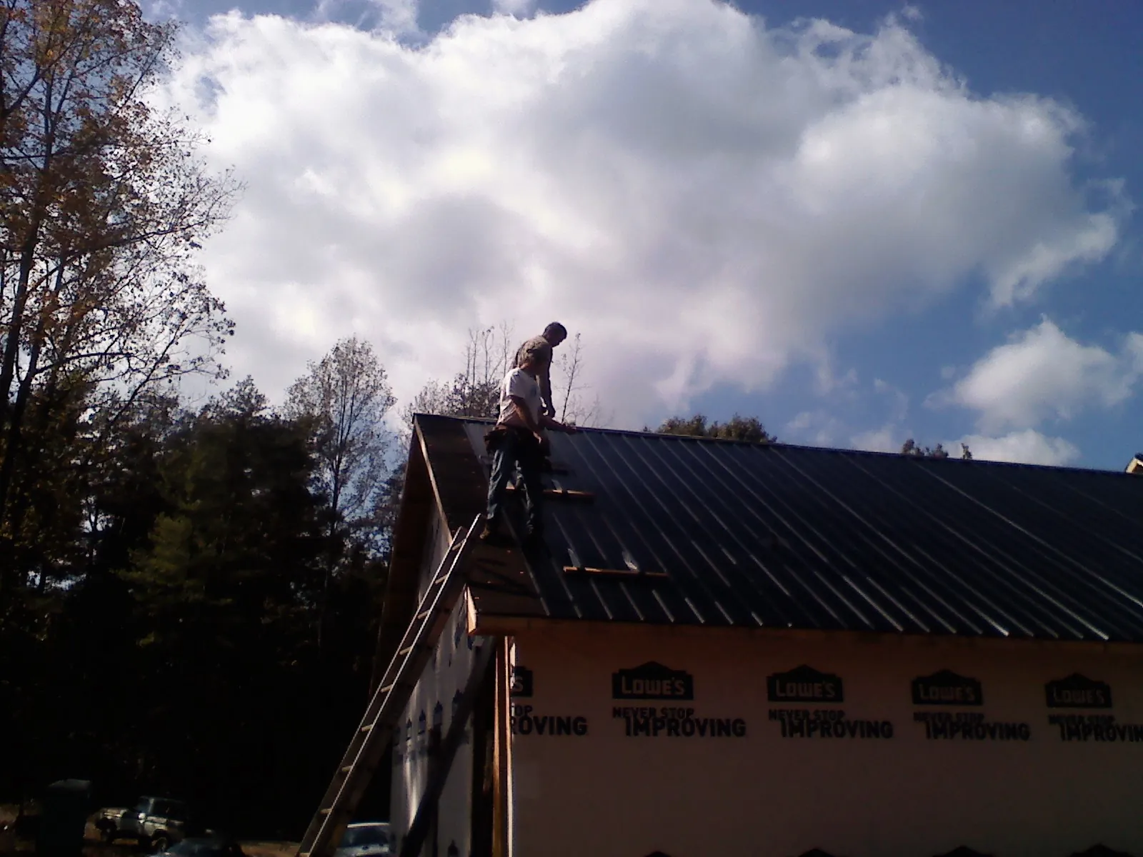 Roofer fastening dark metal panels high against a cloudy sky, from a Roof Inspection job in Ionia