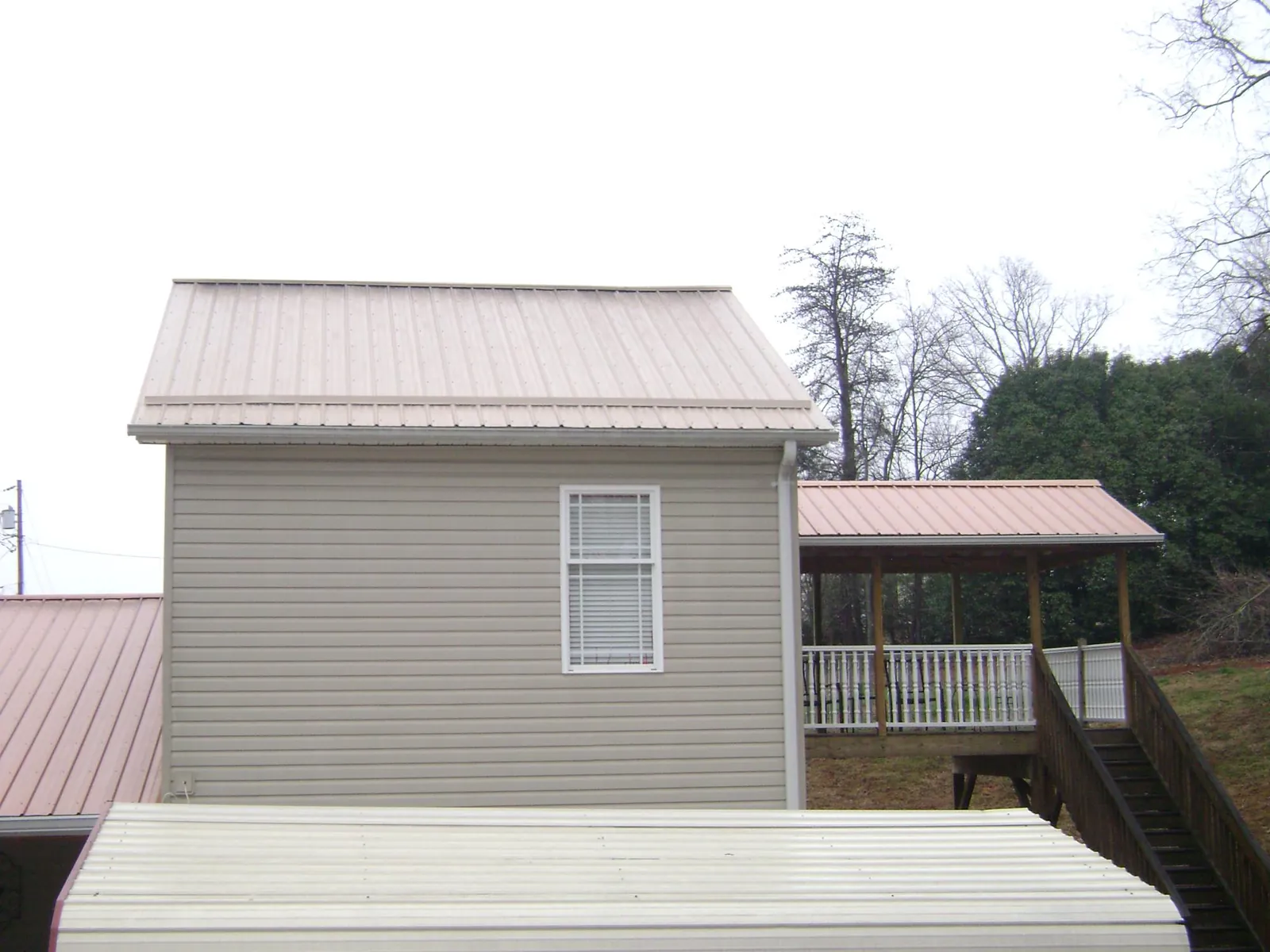 Tan metal roofs on a two story addition and attached porch, from a Roof Replacement job in Ionia